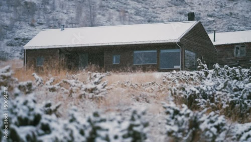 A modern wooden cabin at the Turtagro, Norway. The light first snow is falling covering the ground, trees, bushes, and withered grass. Slow-motion, pan left. photo
