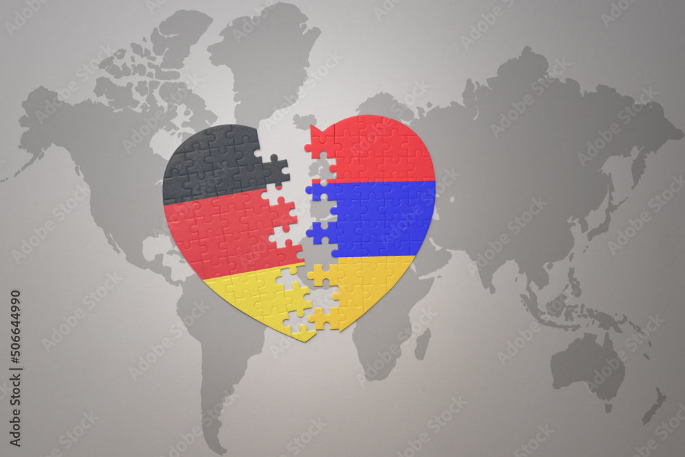 Naklejka premium puzzle heart with the national flag of armenia and germany on a world map background. Concept.