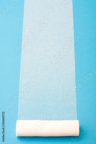 Sterile bandage roll unwound on blue background.