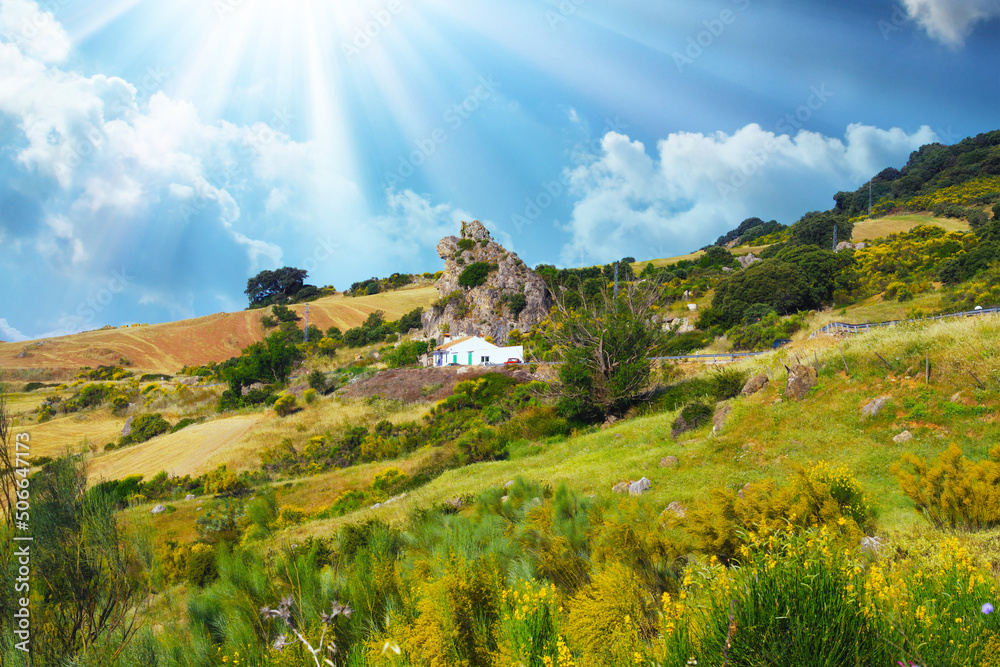 Typical andalusian calm mountainside valley landscape, sun rays, low morning clouds, idyllic white farm house in rock front, agricultural fields - Spain, Andalusia