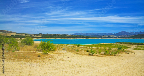 Beautiful idyllic calm blue turquoise mountain swimming lake, empty sand beach - Reservoir Vinuela, Malaga area, Spain