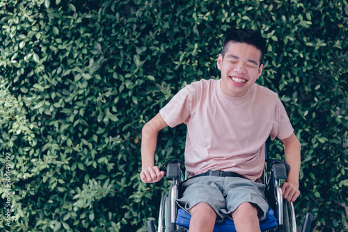 Young man with disability with happy face by with cheerfulness in nature green background, Teenager boy sitting with tray for activities on wheelchair, Good mental health and positive picture concept.