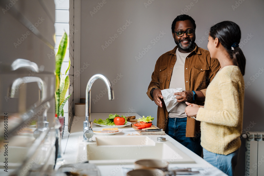 Black bearded man smiling while making sandwiches with his daughter Black bearded man smiling while making sandwiches with his daughter