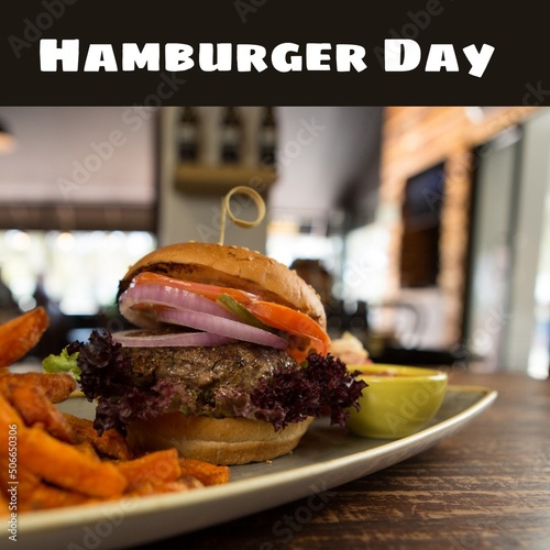 Composite of hamburger day text with burger and french fries in plate, copy space