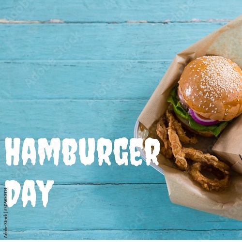 Overhead view of hamburger day text by burger on blue table, copy space