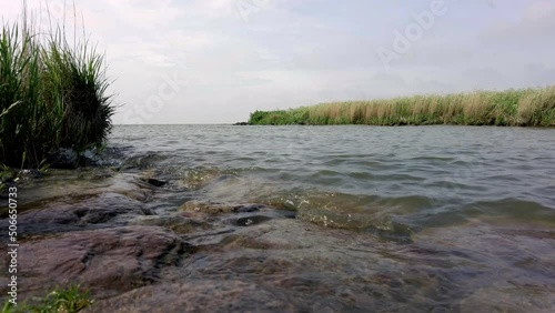 4K timelapse at the mouth of a river, with a low angle view of a lake with small waves, reeds and rocks in the foreground and background, with clouds passing by. Dutch bird sanctuary nature reserve photo