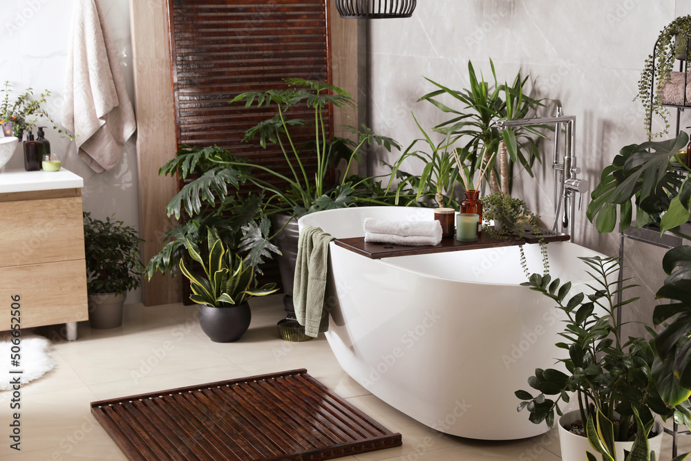 Modern white tub and beautiful green houseplants in bathroom. Interior design Modern white tub and beautiful green houseplants in bathroom. Interior design