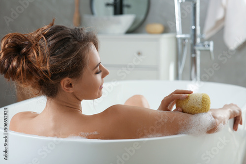 Tela Beautiful woman with sponge taking bath indoors