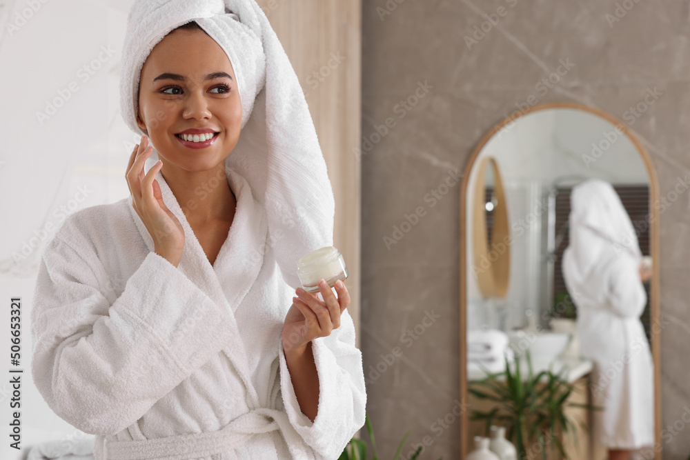 Beautiful African American woman applying cream onto face in bathroom, space for text - obrazy, fototapety, plakaty 