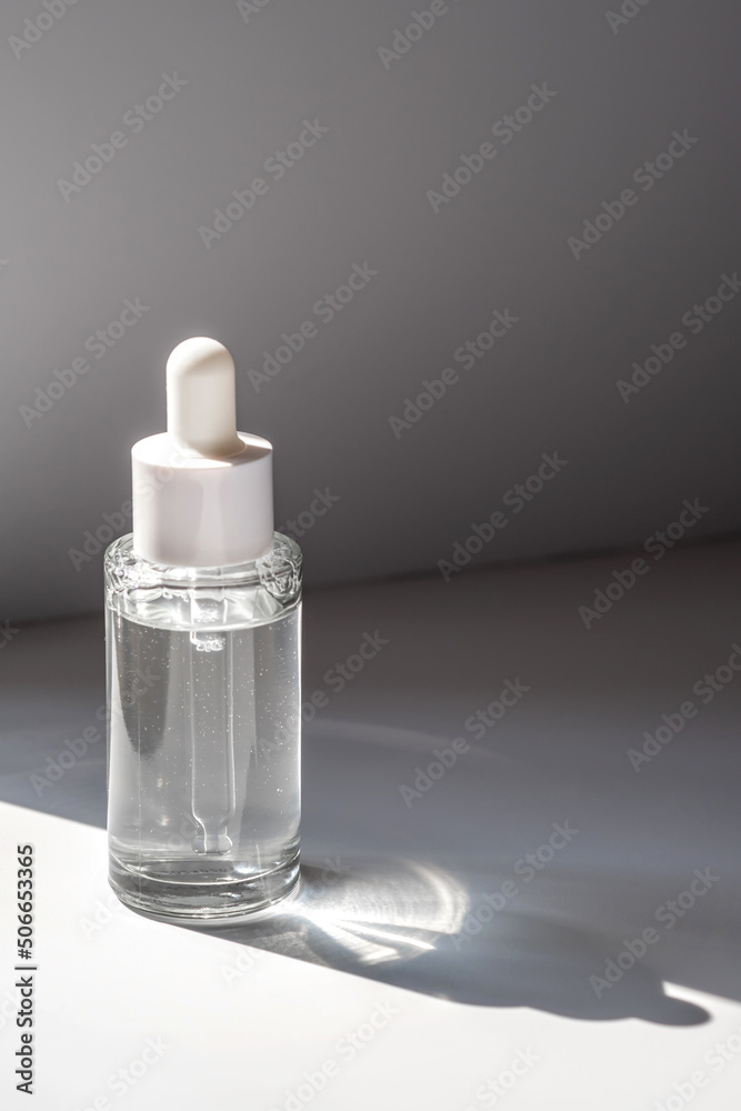 A white transparent bottle with serum in the rays of the sun. A white transparent bottle with serum in the rays of the sun.