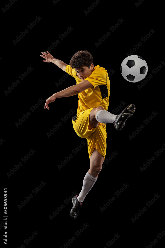 Dynamic portrait of professional football, soccer player training with ball isolated on dark background. Concept of sport, match, active lifestyle, goal and hobby