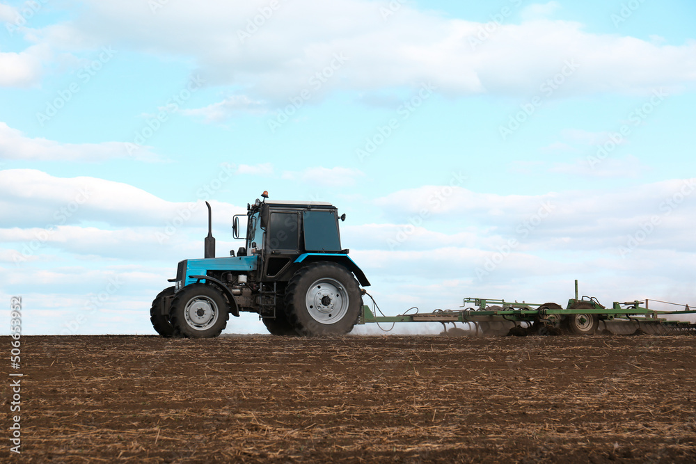 Tractor with planter cultivating field on sunny day. Agricultural industry