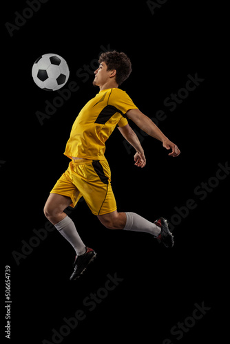 Dynamic portrait of professional football, soccer player training with ball isolated on dark background. Concept of sport, match, active lifestyle, goal and hobby
