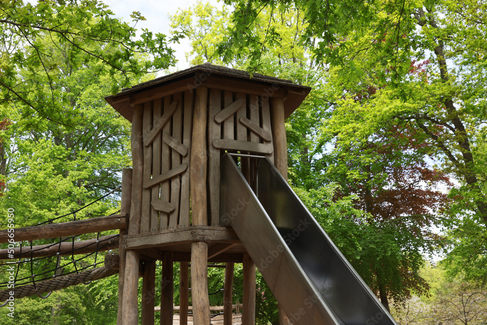 Wooden slide with bridge near big trees in park. Outdoor playground
