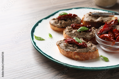 Slices of bread with delicious pate, sun dried tomatoes and basil on wooden table. Space for text