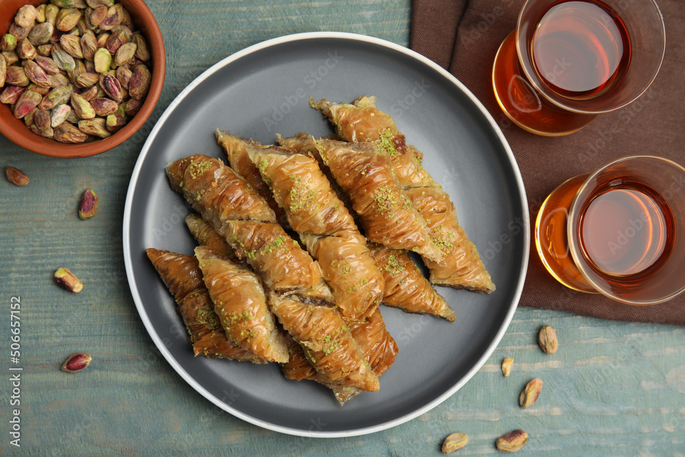 Delicious baklava with pistachios, scattered nuts and hot tea on light blue wooden table, flat lay Delicious baklava with pistachios, scattered nuts and hot tea on light blue wooden table, flat lay