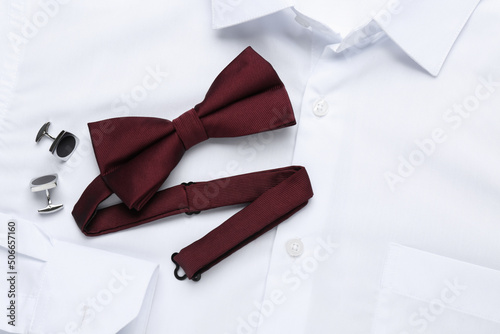 Stylish burgundy bow tie and cufflinks on white shirt, top view photo