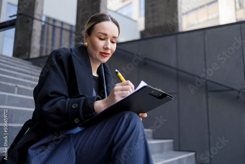 Business woman writing on clipboard outdoors