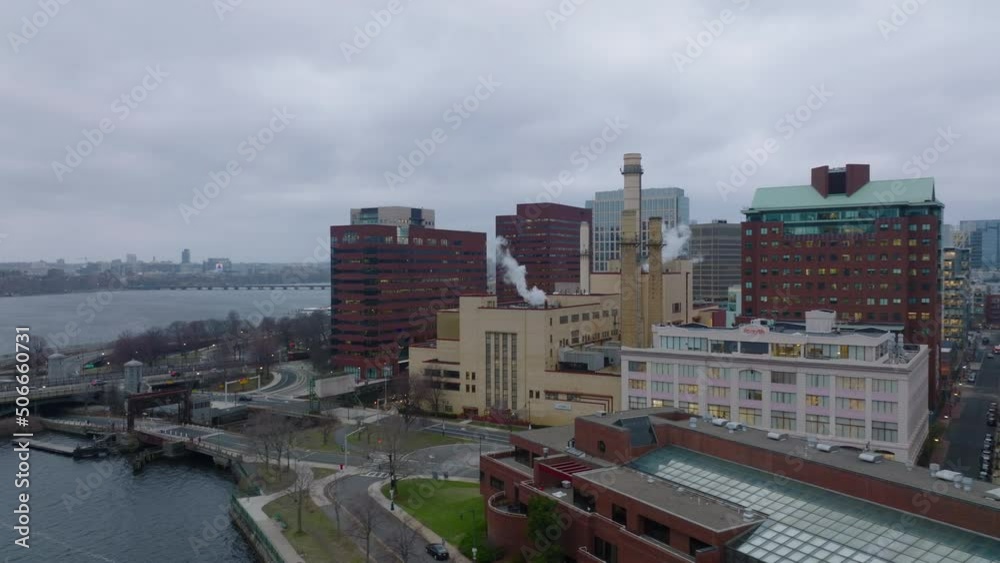Slide and pan shot of factory or heating station with chimneys on riverbank. Buildings in urban borough. Boston, USA
