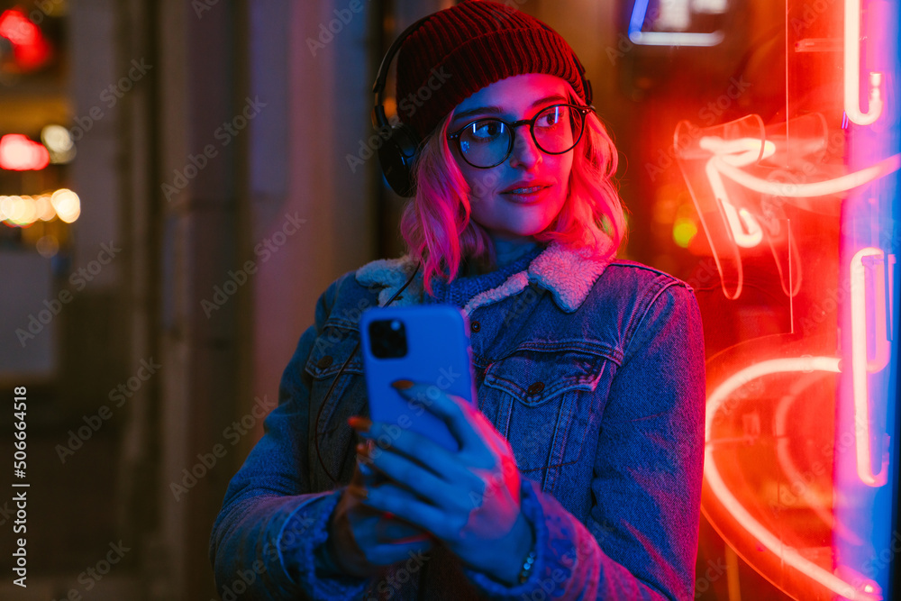 Young woman listening music and using cellphone at city street