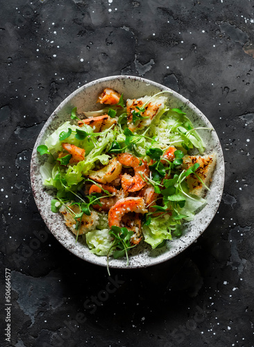 Caesar salad with grilled shrimp on a dark background, top view