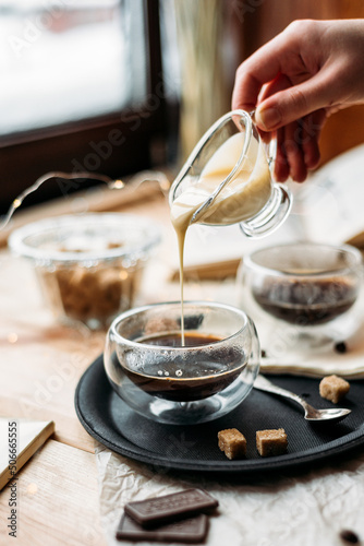 Fotografiet Espresso in a glass cup hand pours condensed milk - cane sugar