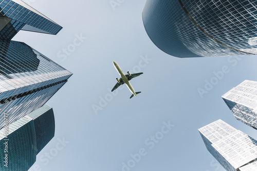 Business city center buildings with flight plane background. Modern office architecture in the financial district. Glass skyscrapers in sunny weather. Economy, money, development, market concept.