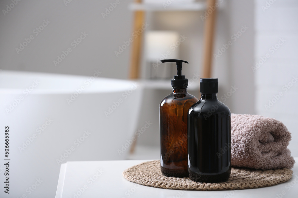 Bottles of bubble bath and towel on white table in bathroom, space for text