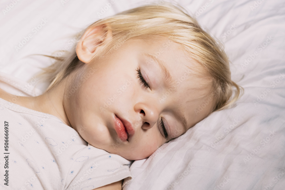 Portrait of a little boy sleeping on white pillow. Sleeping beauty. Beautiful baby Child with long blonde hair is lying. Close-up face. Cute toddler kid. Pastel tones. Authentic candid lifestyle. Portrait of a little boy sleeping on white pillow. Sleeping beauty. Beautiful baby Child with long blonde hair is lying. Close-up face. Cute toddler kid. Pastel tones. Authentic candid lifestyle.