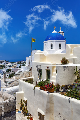 White church with a blue dome on Santorini island in Greece. Hot summer sun day.