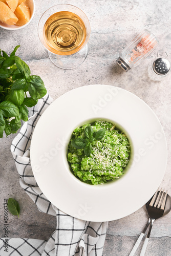 Italian risotto. Delicious risotto in white plate with pesto sauce or wild garlic pesto, basil, parmesan cheese and glass of white wine on old light grey table background. Top view with copy space.