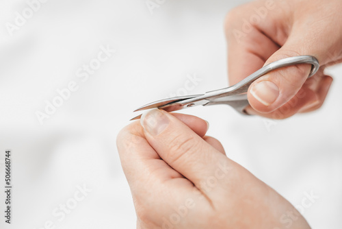 Nail care at home. A woman s hand cuts nails with manicure scissors on a white background. Nail hygiene. Hand care. copy space