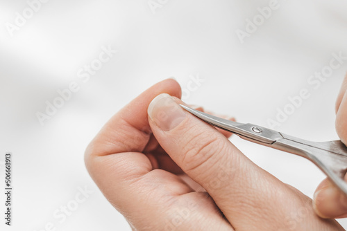 Trims cuticles on fingers. Home manicure. A woman's hand cuts nails with manicure scissors on a white background. Nail hygiene. Hand care photo