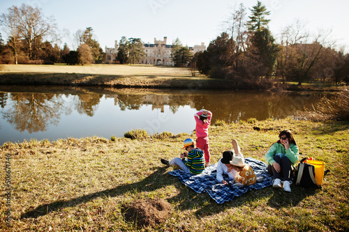 Mother with four kids having picnic near pound at Lednice park against castle, Czech Republic.