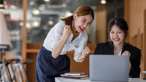 Euphoric winner watching a laptop on a desk winning at working in an office, Asian Teamwork, coworker cooperation, financial marketing team, or corporate business employee concept.