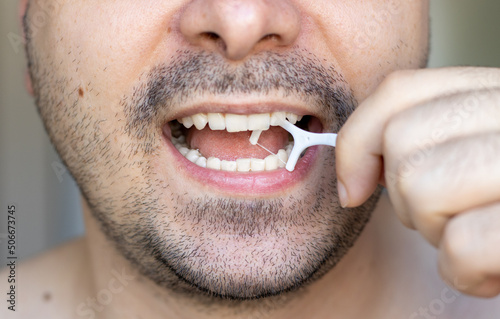 young man is cleaning his teeth with a toothpick. plastic dental floss. close up photo of mouth. stomatological concept. dental care, family education. Beard man