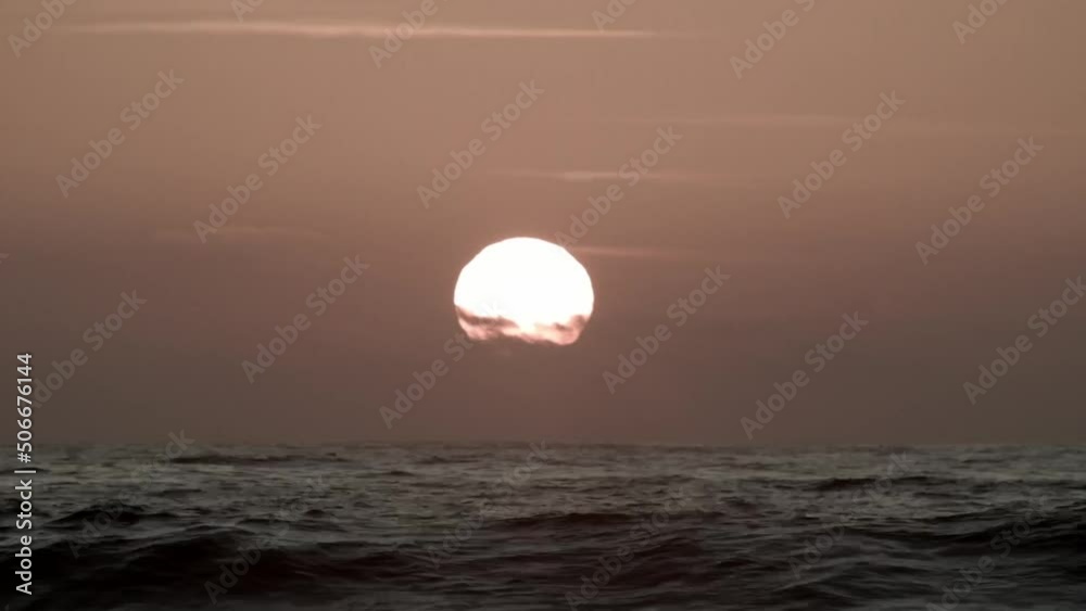 Surfer Paddles In The Ocean With Round And Bright Sun Setting In The Sky At The Beach In Atacama, Chile. - Static Surfer Paddles In The Ocean With Round And Bright Sun Setting In The Sky At The Beach In Atacama, Chile. - Static