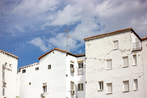 Front view of old residential white houses against blue sky in nice day. Beautiful postcard of a city from a trip. Vintage Spanish architecture. Historic Quarter in town of Portugal. Cracked facades.