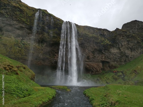 A foss waterfall in iceland with a grey sky and green grass around the river water flow on a roadtrip brak stop vacation © Simon
