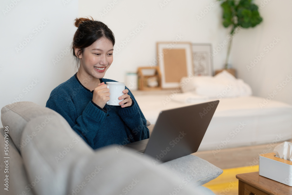 Happy beautiful woman watching videos or online webinar on a laptop sitting on the sofa in the house - online education concept