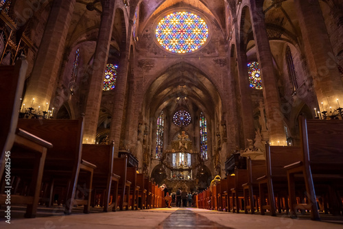 Mallorca, Spain. April 27, 2022. Low angle view of stained glass ceiling and pews in medieval La Seu Cathedral. Tourists praying at beautiful gothic church. Interior of historic religious place. photo