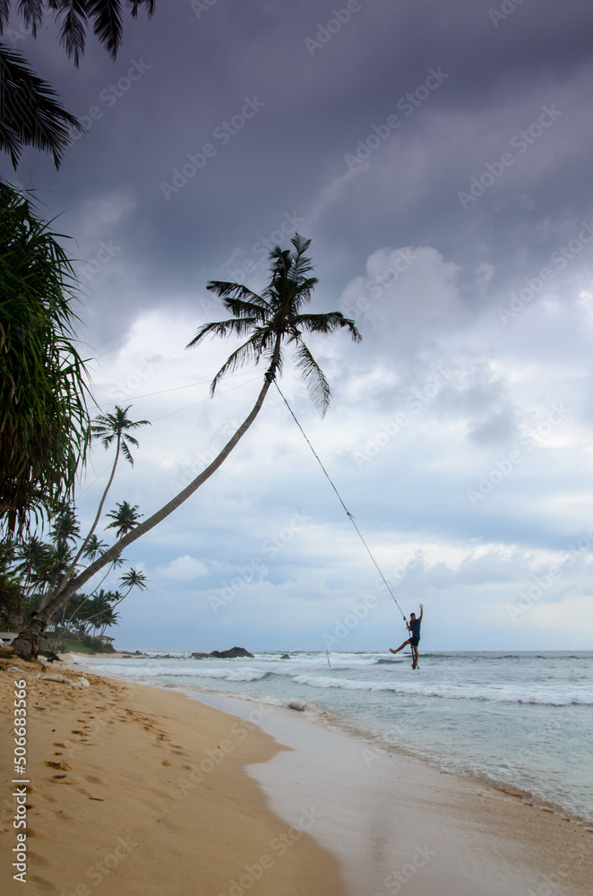 A man swings on the palm over the ocean before a storm in the south of Sri Lanka
