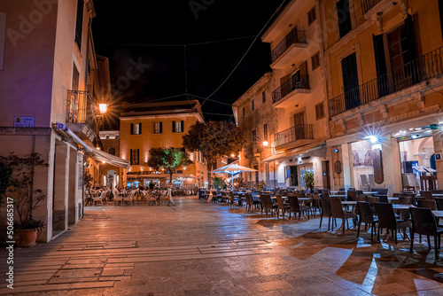 Mallorca, Spain. April 27, 2022. Illuminated outdoor restaurants and cafe at townsquare. Hotel buildings with place setting in city against sky. View of town during night.