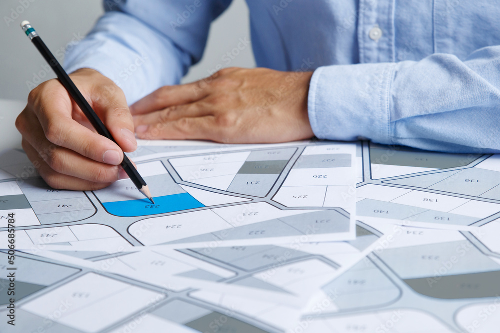 Man holding a pencil pointing to cadastral map to decide to buy land. real estate concept with vacant land for building construction and housing subdivision for sale, rent, buy, investment Man holding a pencil pointing to cadastral map to decide to buy land. real estate concept with vacant land for building construction and housing subdivision for sale, rent, buy, investment