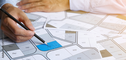 Man holding a pencil pointing to cadastral map to decide to buy land. real estate concept with vacant land for building construction and housing subdivision for sale, rent, buy, investment photo