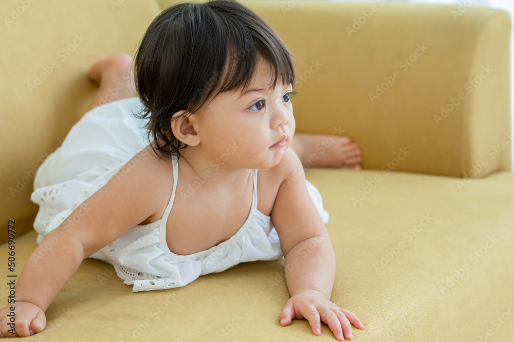 Selective focus adorable caucasian little baby daughter girl, crawling on sofa, playing in comfortable living room at home or house with happiness. There is copy space. Kid Development Concept. Selective focus adorable caucasian little baby daughter girl, crawling on sofa, playing in comfortable living room at home or house with happiness. There is copy space. Kid Development Concept.
