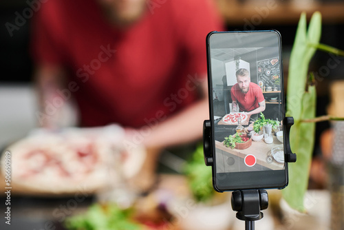 Selective close-up shot of Caucasian food blogger filming delicious pizza cooking process on smartphone camera photo