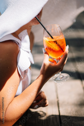 Perfect summer day: beautiful girl legs in the blue clean swimming pool water with refreshing orange cocktail