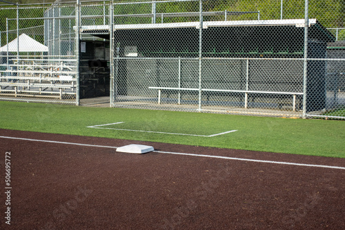 Angled view of a white base on a baseball field, with the view of a dugout in the background