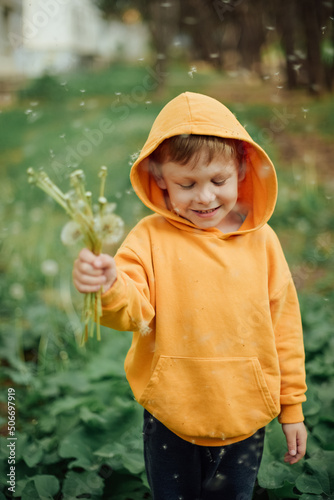 A little boy in a yellow sweatshirt blows on a bouquet dandelions.
